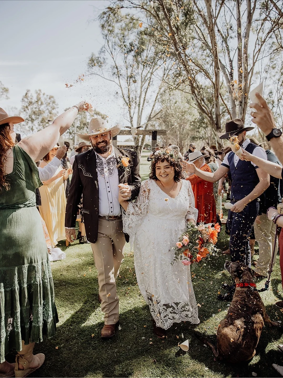 Wedding guests throwing confetti around the couple, with their dog beside them