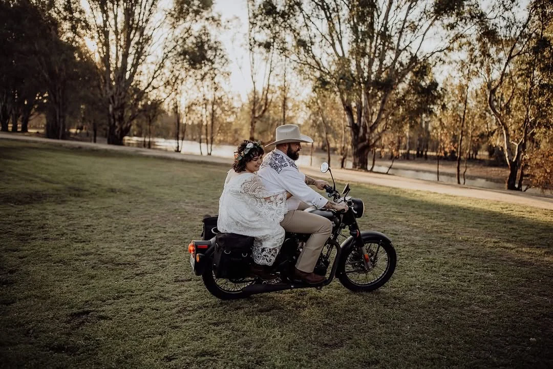 A couple riding across the lawns beside the lagoon on their wedding day